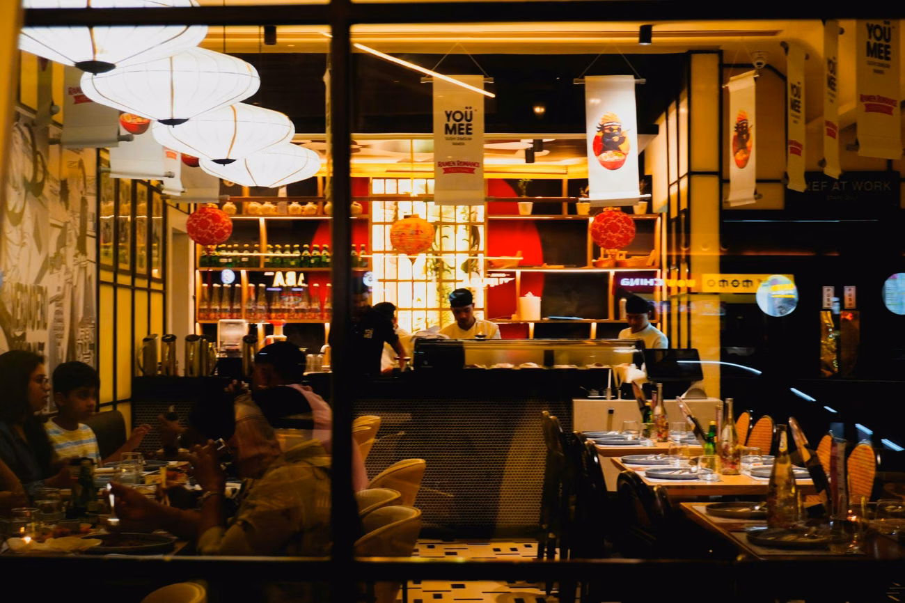 A restaurant dining room busy in the evening, seen from the street through the window